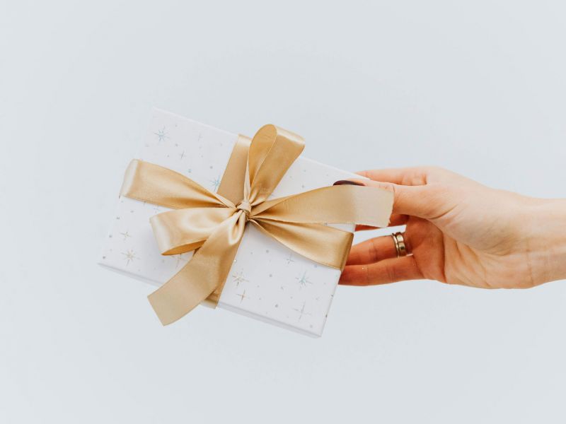 Symbolbild: Hand hält einen Geschenkgutschein mit goldener Schleife